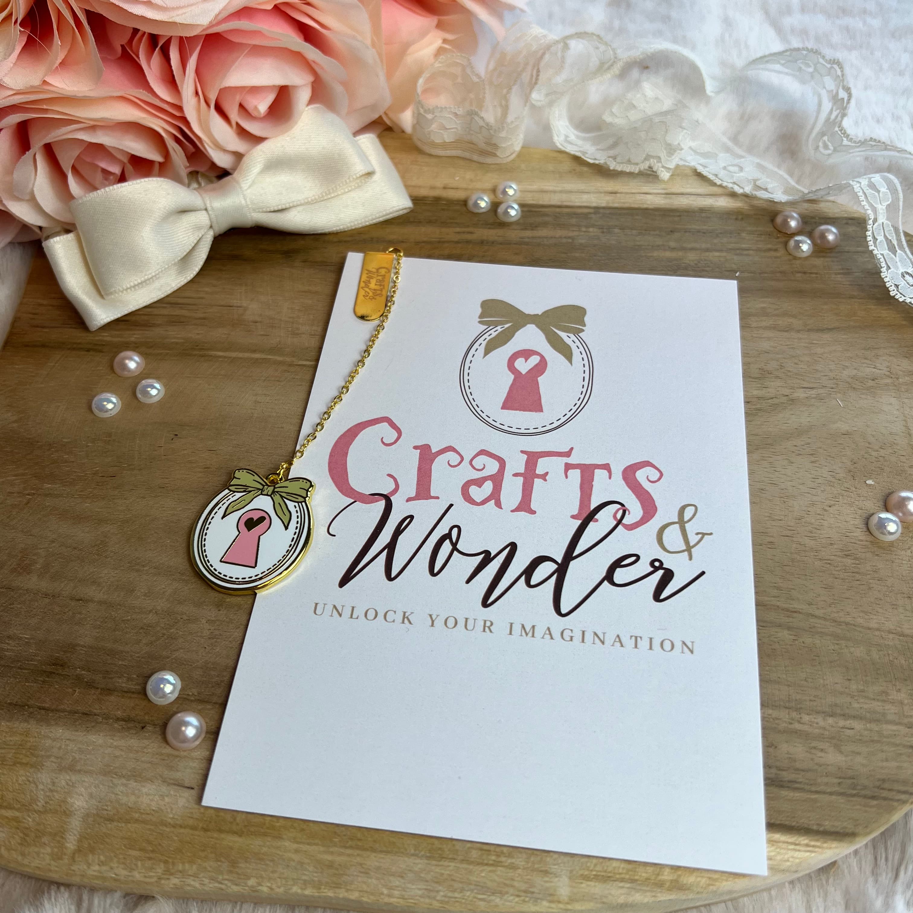 The Crafts & Wonder charm on a vintage wooden surface with roses and pearls